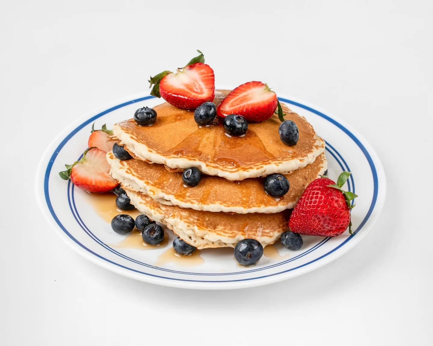 A fluffy pancake stack topped with strawberries, blueberries, butter, and maple syrup