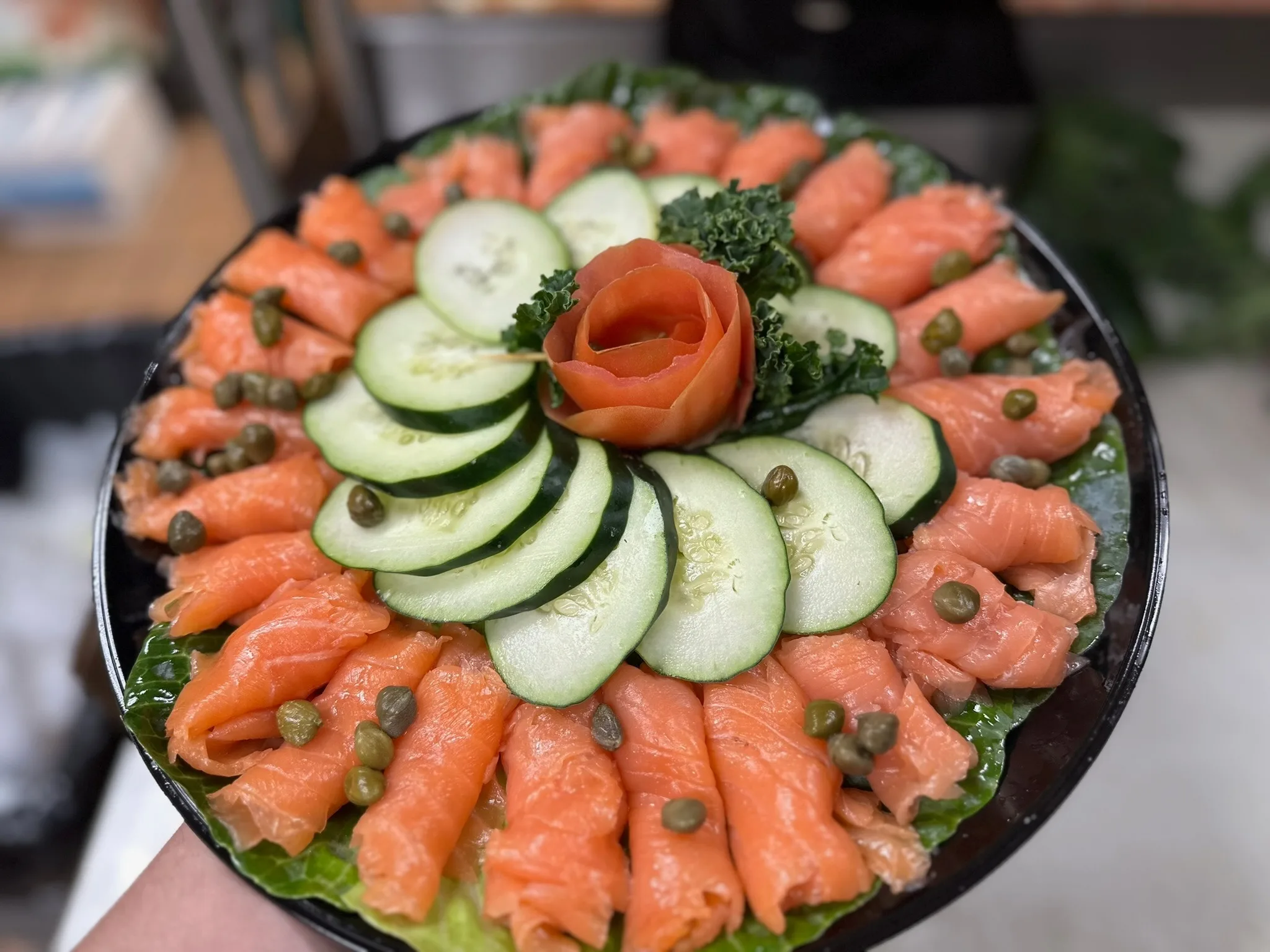 Hand-sliced Nova lox platter — silky lox arranged around cucumber with capers and a tomato rose